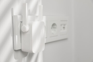 Wireless Wi-Fi repeater on white wall indoors, space for text