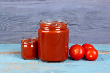 Jars with tasty tomato paste on blue wooden background