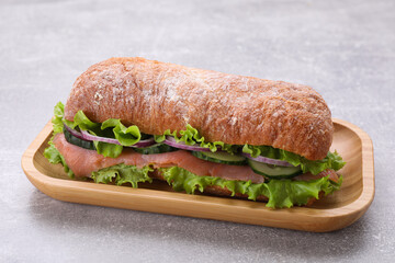 Delicious sandwich with fresh vegetables and salmon on light gray table