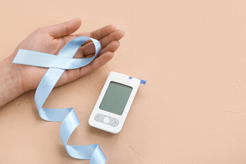 Woman with awareness ribbon and glucometer on beige background. Diabetes concept