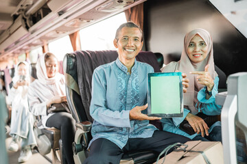 mature muslim couple using showing blank tablet screen to camera while riding a bus