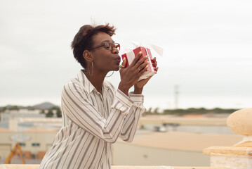 a dark-skinned african girl with glasses holds a gift box in her hands and kisses it, rejoices at the gift on the terrace