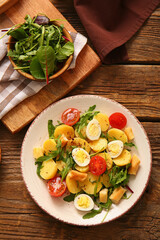 Plate of tasty potato salad with eggs and tomatoes on wooden background, top view