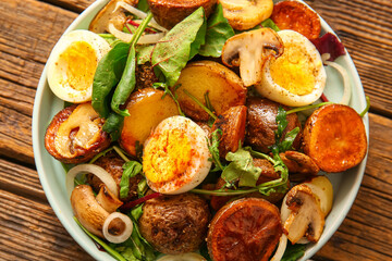 Plate of tasty potato salad with eggs and mushrooms on wooden background, top view