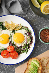 Plate with tasty fried eggs, salad and avocado sandwich on grey background