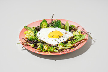 Plate with tasty fried egg and salad on grey background