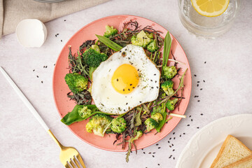 Plate with tasty fried egg and salad on grey background