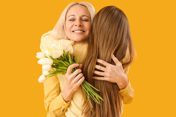 Mature woman with tulips hugging her daughter on orange background. Mother's Day celebration