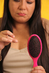 Latin adult woman with very long straight hair suffers from hair loss looking at the brush how many...