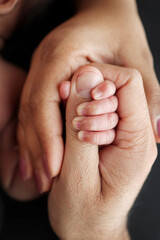 Fototapeta premium Close-up of the small hand of the child and the hand of the mother and father. A newborn baby after birth clings tightly to the finger of its parents. Professional macro photo on black background