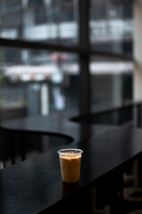 A cup of iced coffee sits on a black counter in front of a window.