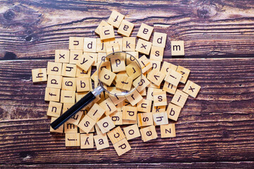 English alphabet made of square wooden tiles with the English alphabet scattered on table background. The concept of thinking development, grammar. Magnifier placed on English letters