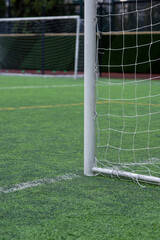 A white aluminum goal with a white net for youth’s football tournament on artificial plastic grass pitch in the morning waiting for teams to play and practice. Another white goal in a background.