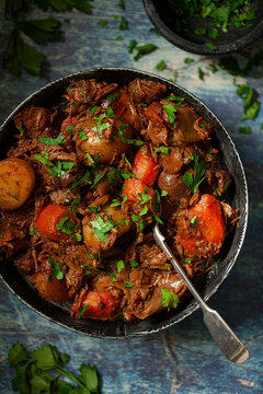 Beef stew in a metal bowl with carrot and potato and garnished with chopped parsley.