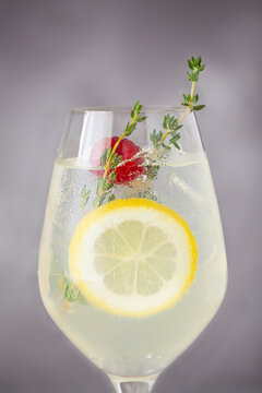 Close up of a wine glass with a lemon spritz cocktail in it garnished with a lemon slice, raspberry and fresh thyme.
