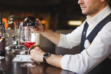Faceless sommelier pours red wine into stem glass.