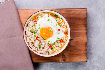 Instant noodles or ramen with minced pork and boiled egg in white bowl on the table with copy space - top view