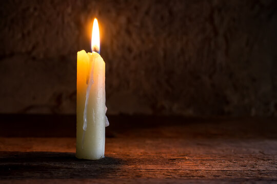 A burning candle on a rough wooden shelf. A lit candle in the twilight.