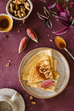 Crepes, folded on a handmade ceramic plate,  decorated with figs, caramel and walnuts over a purple background