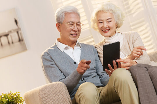 Elderly couple sitting on sofa using tablet