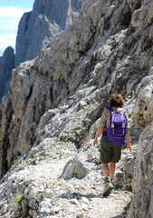 Young female hiker walks with backpack on stony path on alps in Northern Italy in summer