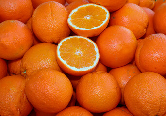 background of many ripe orange oranges and two halves open to see the juicy contents for sale at the greengrocer