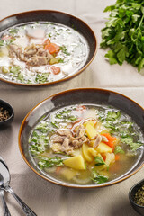 two deep green bowls with traditional european chicken soup with potato, carrots, celery, fresh parsley on a beige colored kitchen table cloth