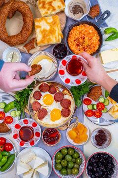Traditional Turkish breakfast table. Eggs with sujuk, vegetables, jams, olives and cheese on it. Woman and man enjoying Turkish foods and tea.