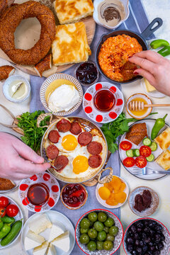 Traditional Turkish breakfast table loaded with eggs, sujuk. menemen, olives, kaymak, honey, simit, borek, vegetables. Man and woman taking food top view.