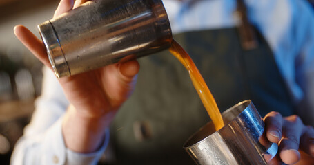 Cool experienced bartender mixing an alcohol beverage in a shaker. Authentic barman pouring cocktail drink with various ingredients - food and drink close up 