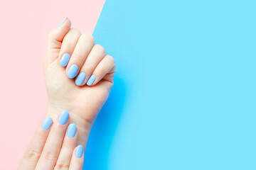 Female hands with light blue manicure on blue and pink background with copy space.
