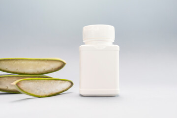 Green Fresh Juicy Aloe Vera Slice With White Plastic Bottle Of Medicine, Herbal Capsule, Pills, Vitamins On Pink Background. Pharmacy, Cosmetics, Natural Medicine, Product. Horizontal Plane, Closeup