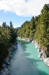 Glacier-fed river gorge lined with by quartz rocks and native rainforest bush under a blue sky in Hokitika, West Coast, New Zealand