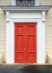 An old, bright orange wooden door with an ornate white frame in Hokitika, West Coast of New Zealand.      