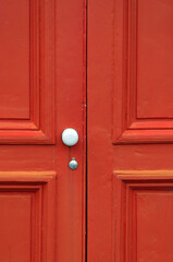 Fototapeta premium Close-up of an old, bright orange wooden door with a white doorknob, in Hokitika, West Coast of New Zealand.
