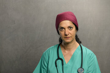 Health professional poses in studio wearing green scrubs, a purple head cover and equipped with a stethoscope.