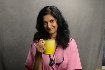 Health professional poses in studio wearing pink scrubs and sipping coffee.