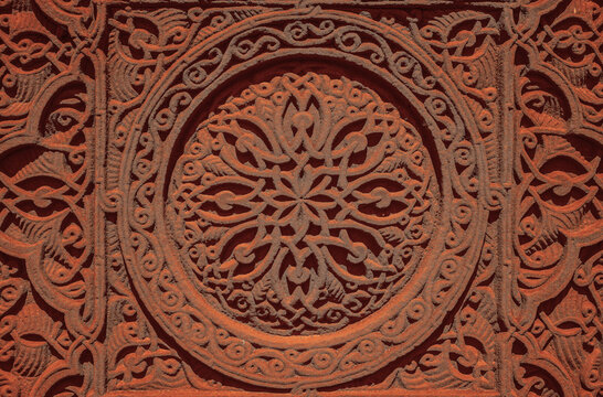 Carved round ornament with intertwining strips forming a pattern placed in a round frame on a red volcanic stone. Traditional tufa stone carving ornament on a wall of Armenian Orthodox Church.