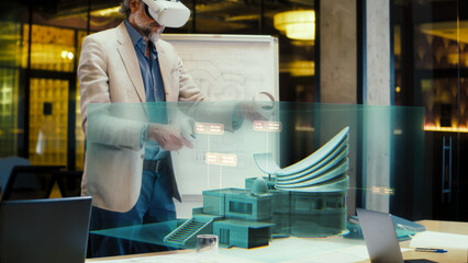 Male designer uses VR headset and wireless controllers, creates modern building exterior design in virtual reality cyberspace, presents project to coworkers. 3D hologram. Future digital technologies.
