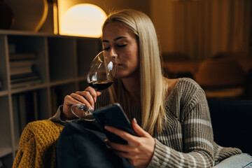 A beautiful blond woman enjoys a glass of red wine in the evening