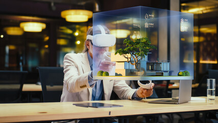 Obraz na płótnie Canvas Male designer uses VR headset and wireless controllers, makes architectural project, creates house exterior design in virtual reality. Modern hi-tech company. 3D hologram. Future digital technologies.