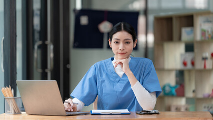 An Asian female doctor works with a laptop at a desk in a hospital, health care and preventing disease concept.