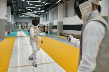 Two swordsmen wearing uniform fighting duel during training in sport gym room