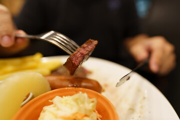 Man eating Grilled Meats stake from plate. hand holding knife and fork cutting grilled beef steak