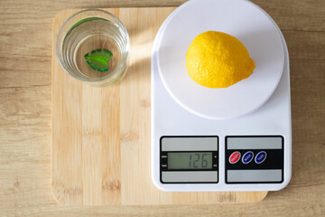 Fresh lemon on a white kitchen scale, a glass of water on the kitchen table. The concept of proper nutrition and healthy lifestyle