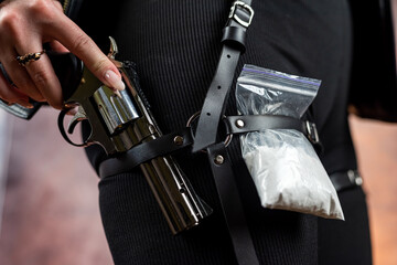 female drug addict wear dark black clothes holding  gun pistol and package with white powder
