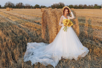 Wedding portrait. A red-haired bride in a white dress, holding a bouquet of sunflowers, on the background of a field. Beautiful curls. Sincere smile. Elegant dress. Yellow flowers