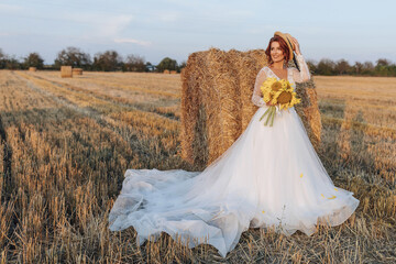 Wedding portrait. A red-haired bride in a white dress, holding a bouquet of sunflowers, on the background of a field. Beautiful curls. Sincere smile. Elegant dress. Yellow flowers