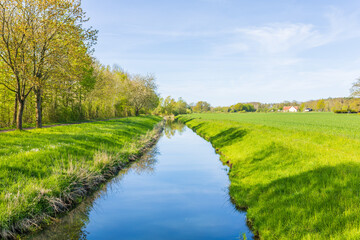 Bach fließt durch eine idyllische Landschaft mit Waldrand und Feldern