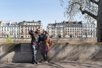 Family with one little girl taking a selfie with beautiful Parisian buildings on the background...